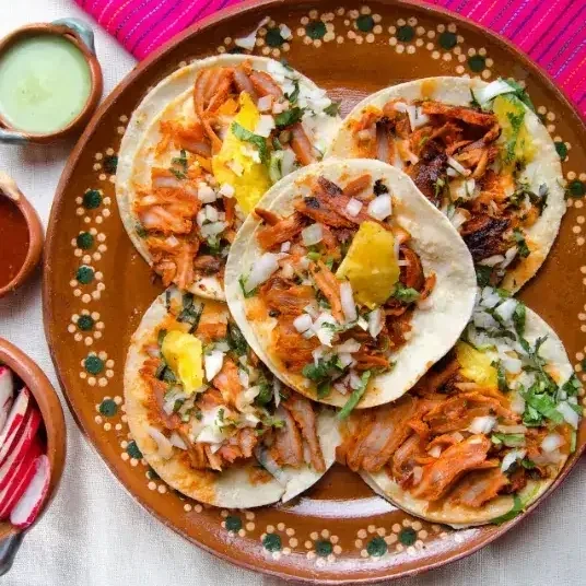 Al pastor tacos on a clay plate with onion, cilantro and pineapple
