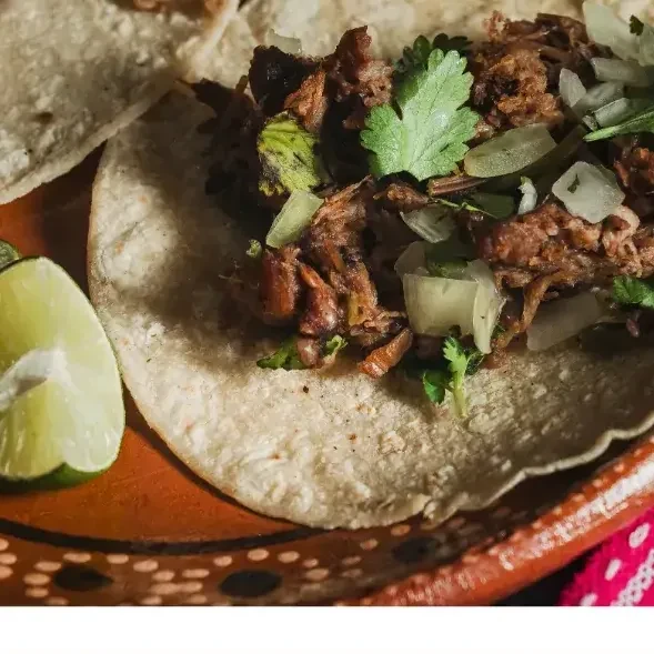 Barbacoa tacos on a clay plate with lime